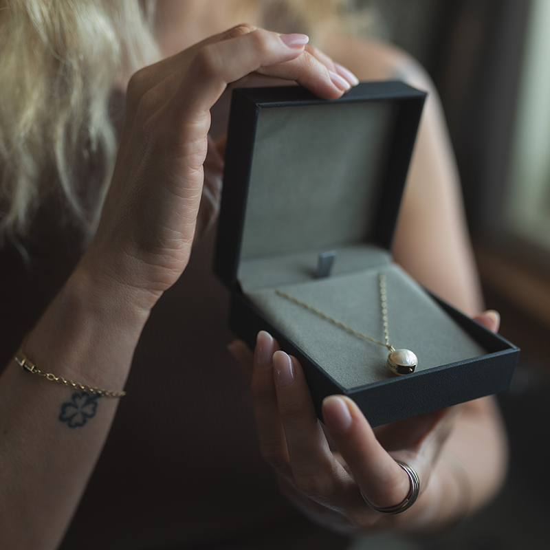 Woman holding a necklace gift box with a Hebrew-engraved pendant